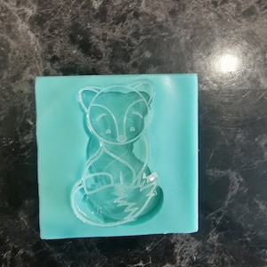 Peut inclure: Un moule en silicone bleu clair avec un motif de renard transparent. Le renard est assis avec sa queue enroulée autour de son corps.