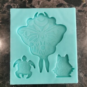 May include: A teal blue silicone mould with three designs: a butterfly with intricate details, a turtle, and a cat. The mould is used for making resin crafts.