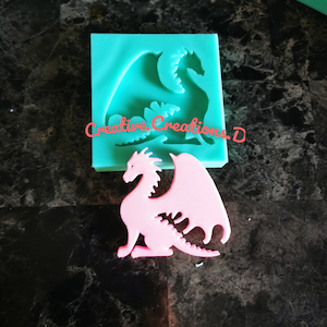 May include: A pink dragon silicone mould with a pink dragon casting. The mould is teal green and has the text "Creative Creations. D" on it.