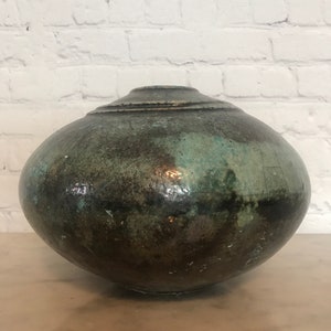 May include: A large, round, green and brown ceramic vase with a textured surface.
