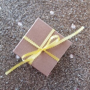 Puede incluir: Una caja de regalo marr&oacute;n con una cinta amarilla atada en un lazo. La caja est&aacute; sobre una superficie dorada brillante.
