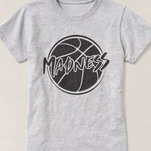 May include: Gray t-shirt with a black basketball graphic and the word "MADNESS" written in a stylized font.