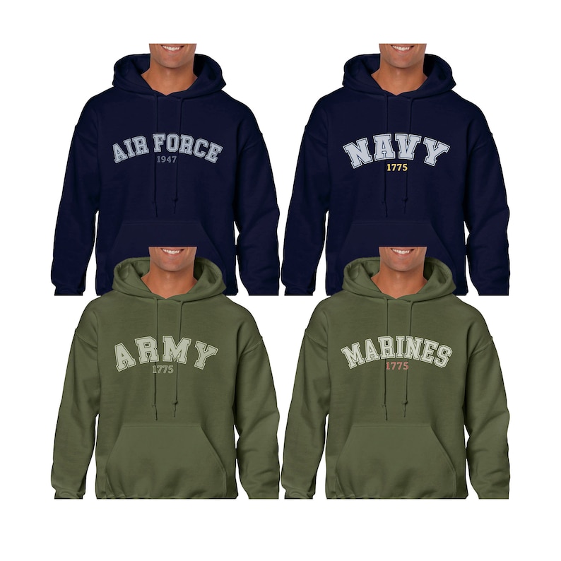 K&ouml;nnte beinhalten: Vier Kapuzenpullover in verschiedenen Farben mit den Namen der Zweige des US-Milit&auml;rs auf der Vorderseite. Die Pullover sind marineblau, olivgr&uuml;n und dunkelgr&uuml;n. Der Text auf den Pullovern lautet "Air Force 1947", "Navy 1775", "Army 1775" und "Marines 1775".