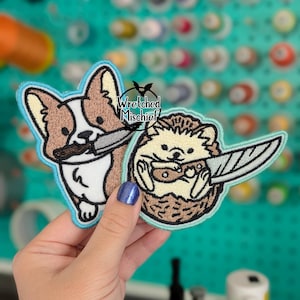May include: Two embroidered patches featuring cartoon animals with knives. One patch is a corgi dog with a knife in its mouth, and the other is a hedgehog holding a knife. The patches have a light blue border and the text "Wretched Mischief".