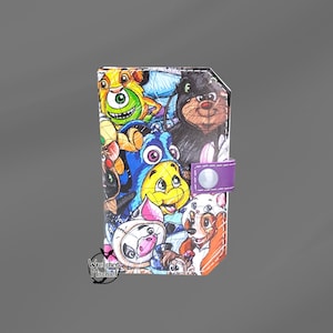 May include: A colorful wallet featuring a collage of cartoon characters. The wallet has a purple strap with a silver snap closure. The design includes a variety of animated figures in bright colors. The words "Wretched Mischief" are printed on the bottom left.