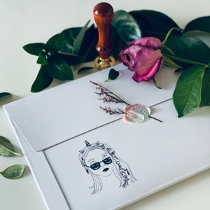 May include: A white envelope with a wax seal and a hand-drawn illustration of a person with a unicorn horn and sunglasses. The text "Nice to meet you" is written around the illustration.