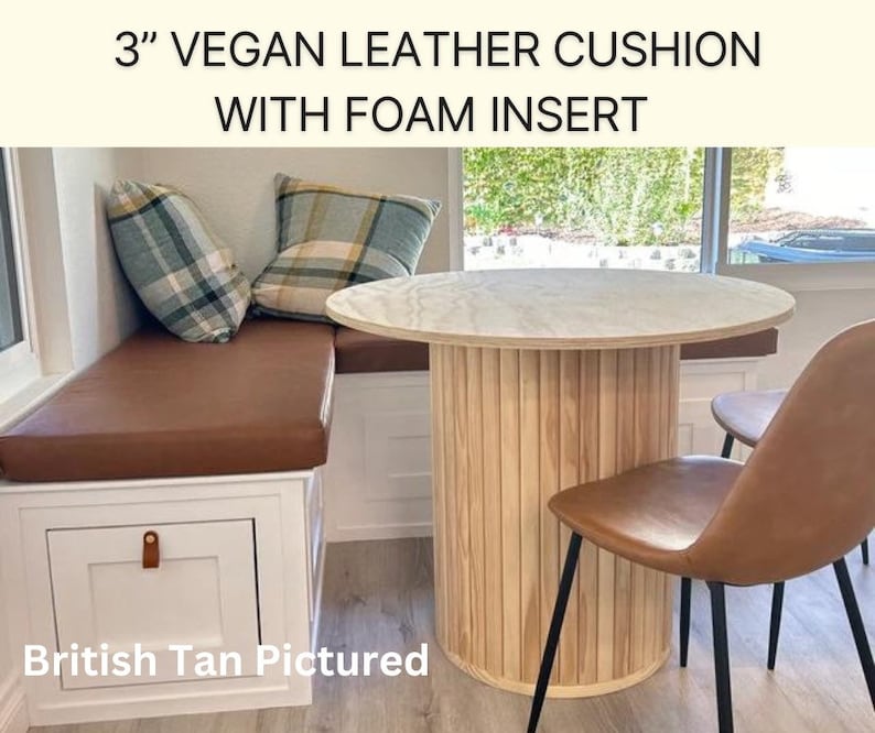 May include: A 3" vegan leather cushion with foam insert in the color British Tan. The cushion is part of a built-in bench seat with a white drawer. The cushion is next to a round table with a white marble top and a wooden base. Two chairs with brown leather seats and black metal legs are next to the table.