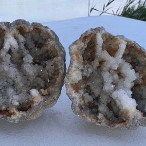 May include: Two halves of a geode with a white crystal interior and a brown, rough exterior.