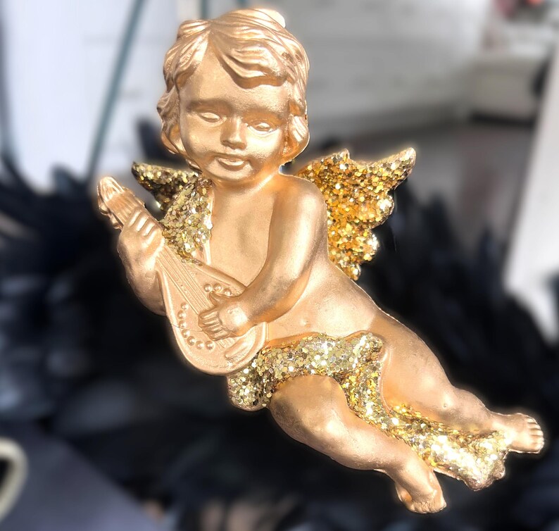 以下が含まれることがあります： 金色のケルビムの置物で、リュートを演奏しています。ケルビムはキラキラ光る翼とアクセントを持っています。この置物は、休日や特別な機会のための装飾品かもしれません。