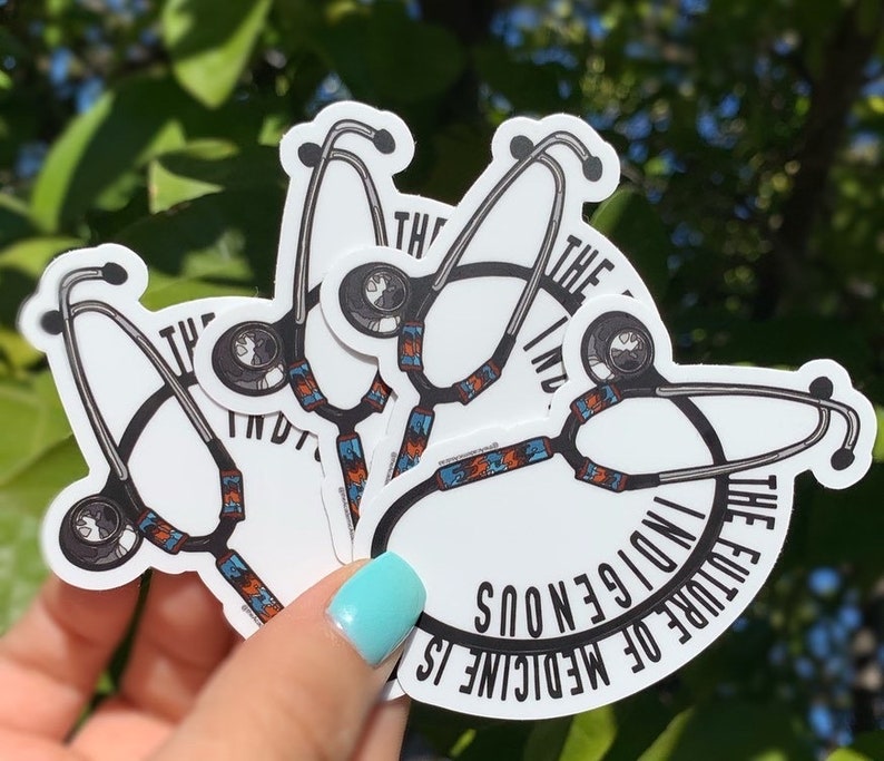 May include: Four white stickers with a black stethoscope design and the text "The future of medicine is indigenous" in a circle around the stethoscope. The stickers are stacked on top of each other.