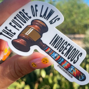 May include: A white sticker with a gavel and the text "The Future of Law is Indigenous" with a colorful design on the handle and the text "@theacademicasdzea" at the bottom.