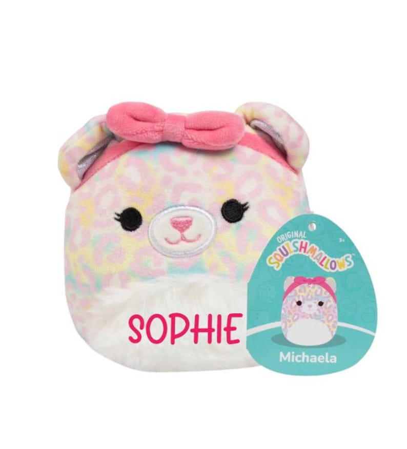 Peut inclure: Un jouet en peluche rose et blanc avec un motif l&eacute;opard et un n&oelig;ud rose. Le jouet a un visage blanc avec des yeux noirs et un nez rose. Le jouet est &eacute;tiquet&eacute; "Sophie" et porte une &eacute;tiquette indiquant "Original Squishmallows Michaela".