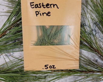 May include: A brown paper pouch with a clear window showing green pine needles inside. The pouch has the text "Eastern Pine" and ".5 oz" written on it.