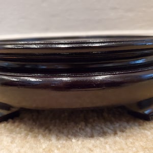 May include: A round, dark brown wooden display stand with a glossy finish. The stand has a tiered design with a flat top and three small feet. The stand is likely used for displaying decorative items.