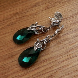 May include: A pair of silver dangle earrings with green crystal teardrop shaped stones. The earrings feature a leaf design and are marked "925" on the back.