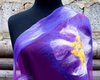 May include: A sheer purple scarf with large, stylized floral designs in white and yellow. The scarf is draped over a black mannequin, showcasing the flowing fabric and intricate flower details. The background is a rustic wooden surface.