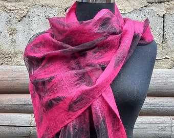 May include: A vibrant pink scarf with black abstract patterns is draped over a black mannequin. The scarf's texture appears soft and fuzzy, with the pink color dominating and the black accents adding contrast. The scarf is a fashion accessory.