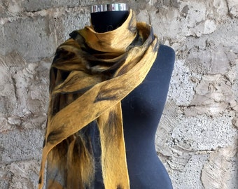 May include: A mustard yellow felt scarf with dark brown leaf-like patterns, draped over a black mannequin. The scarf's design is visible against a textured, gray brick wall.