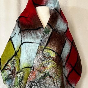 Könnte beinhalten: Ein farbenfroher Schal aus Filzwolle mit einem einzigartigen abstrakten Design. Der Schal weist eine Mischung aus roten, braunen, grünen und blauen Farbtönen auf, wobei schwarze Linien ein Netzwerkmuster bilden. Der Schal wird auf einer Schaufensterpuppe präsentiert.