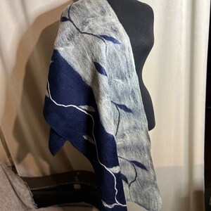 Könnte beinhalten: Ein grauer und marineblauer Filzschal aus Wolle, der über einer Schaufensterpuppe drapiert ist. Der Schal hat ein Blattmuster mit weißen Nähten. Der marineblaue Bereich befindet sich links, der graue Bereich rechts.