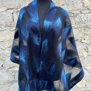 Könnte beinhalten: Ein durchsichtiges, dunkelblaues Tuch mit einem Muster aus hellblauen, federartigen Designs. Das Tuch ist über einer schwarzen Schaufensterpuppe drapiert, was seine offene Vorderseite und fließende Form zeigt. Der Hintergrund ist eine strukturierte, hellfarbige Backsteinmauer.