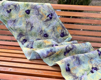 May include: A handmade felt scarf in shades of green, yellow, and purple, draped over a wooden bench. The scarf features a unique design with dark purple accents and intricate patterns, perfect for adding a touch of artistry to any outfit.