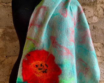 May include: A light blue scarf with a large red and orange flower design. The scarf is draped over a black mannequin and features green and red floral accents. The scarf is made of a soft, textured material.