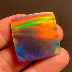 Könnte beinhalten: Ein quadratischer, irisierender Opal-Cabochon mit einem Regenbogen aus Farben, darunter Grün, Blau, Orange und Lila.