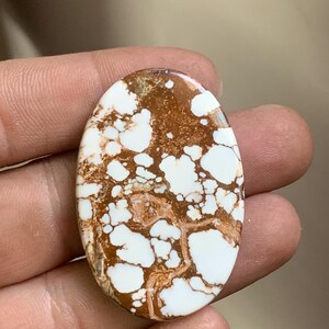 Könnte beinhalten: Ein ovaler Edelstein mit einem einzigartigen Muster aus Weiß und Braun. Die weißen Bereiche sind unregelmäßig und wolkenartig, im Kontrast zur braunen Matrix. Der Stein ist poliert und glatt, was seine natürliche Schönheit hervorhebt. Ideal für die Schmuckherstellung.