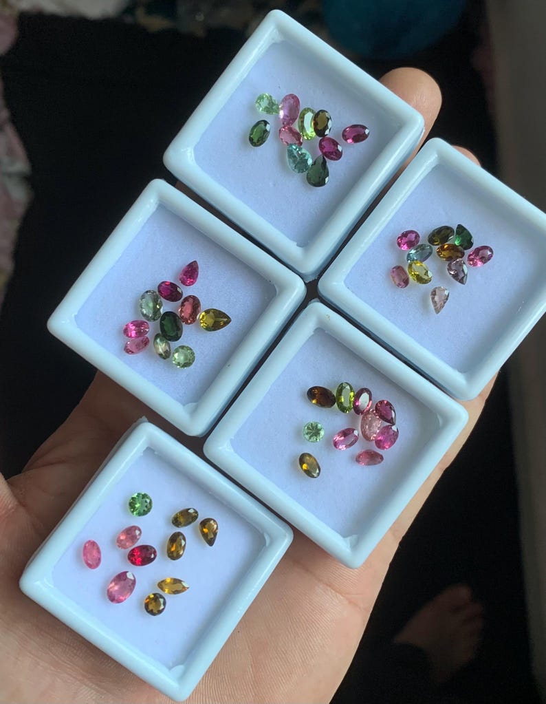 Puede incluir: Surtido de gemas de colores en peque&ntilde;as cajas de exhibici&oacute;n blancas. Las gemas son de varias formas y tama&ntilde;os, incluyendo cortes ovalados, en forma de pera y redondos. Los colores incluyen rosa, verde, marr&oacute;n y amarillo. Las gemas se muestran en una mano.