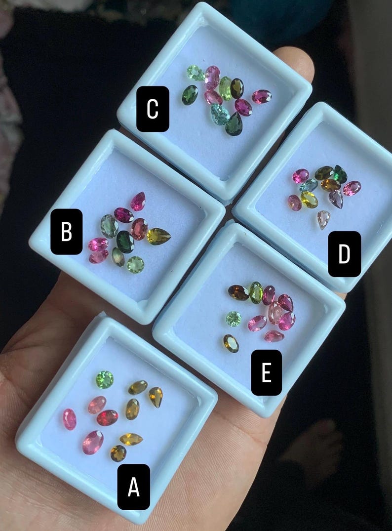 Puede incluir: Una colecci&oacute;n de gemas coloridas exhibidas en peque&ntilde;as bandejas cuadradas blancas. Las gemas var&iacute;an en forma y tama&ntilde;o, con colores que incluyen rosa, verde, amarillo y marr&oacute;n. Las bandejas est&aacute;n etiquetadas A, B, C, D y E.