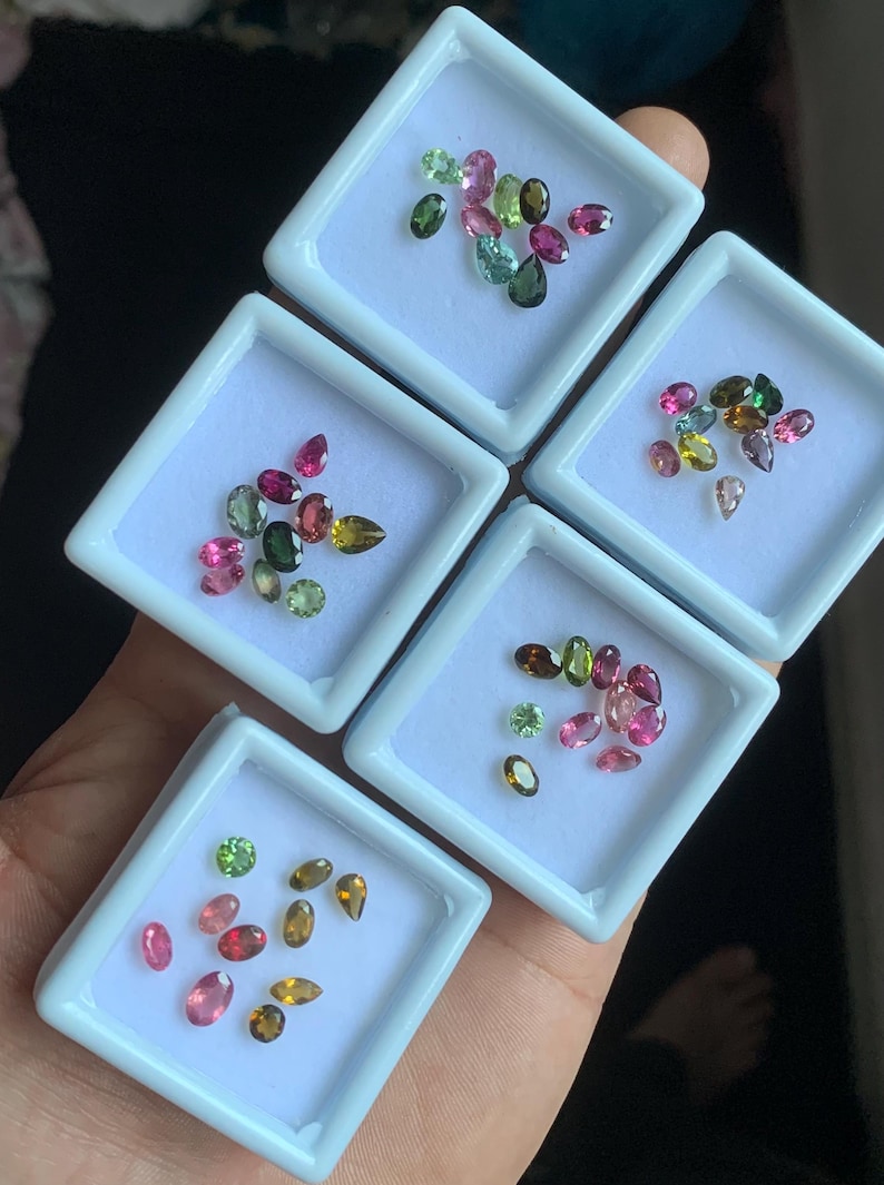 Puede incluir: Surtido de gemas coloridas en peque&ntilde;os recipientes cuadrados blancos. Las gemas son de varias formas y tama&ntilde;os, con colores que incluyen rosa, verde, marr&oacute;n y amarillo. Los recipientes se sostienen en una mano.