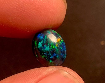 May include: A dark green, blue, and black oval opal gemstone with a high shine.