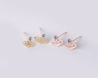 Puede incluir: Un par de pendientes de oro y oro rosa con una pequeña piedra azul y piedras de circonita cúbica blancas en forma de planeta.