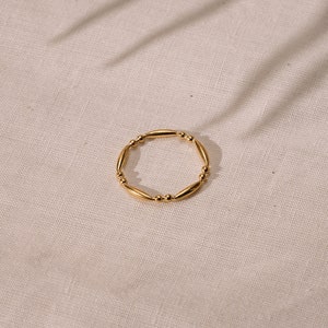 Op de afbeelding: Een gouden ring met een parelmoer ontwerp. De ring is gemaakt van kleine, ronde parels die met elkaar verbonden zijn door dunne, gouden staven.