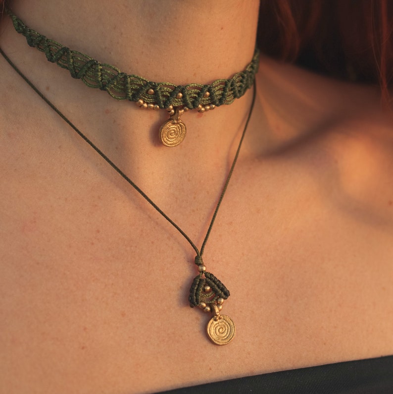 May include: A green macrame choker necklace with a gold pendant featuring a spiral design. The necklace is layered over a simple string necklace with a similar pendant.