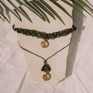 May include: A set of two green macrame necklaces with gold pendant charms. The necklaces are layered on a white surface.