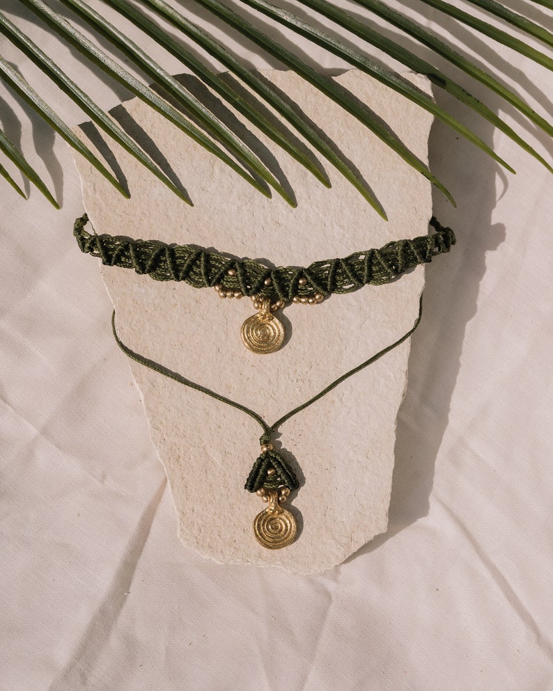 May include: A set of two green macrame necklaces with gold pendant charms. The necklaces are layered on a white surface.