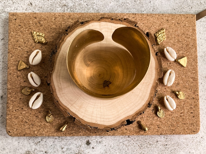 K&ouml;nnte beinhalten: Eine goldene Schale mit einer einzigartigen Form sitzt auf einer Holzscheibe. Die Schale ist von kleinen wei&szlig;en Muscheln und goldenen Anh&auml;ngern umgeben.