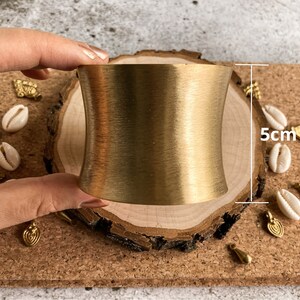 K&ouml;nnte beinhalten: Ein goldfarbenes Metall-Armband mit glatter, geb&uuml;rsteter Oberfl&auml;che. Das Armband ist 5 cm breit und hat eine leicht gebogene Form.