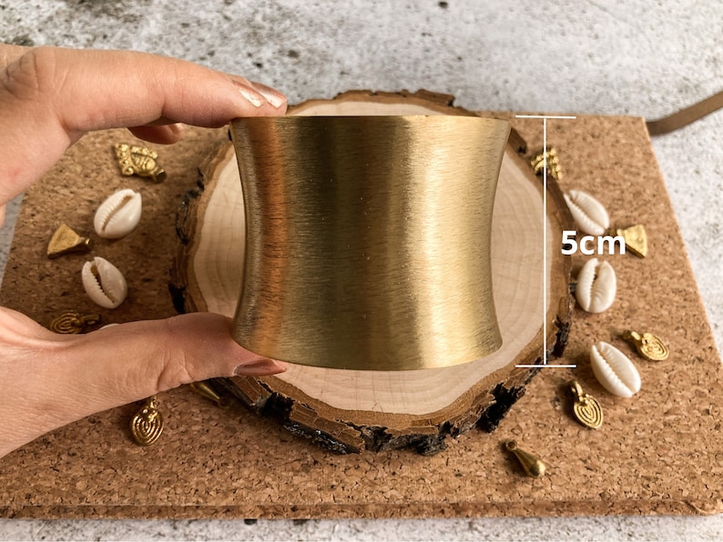 K&ouml;nnte beinhalten: Ein goldfarbenes Metall-Armband mit glatter, geb&uuml;rsteter Oberfl&auml;che. Das Armband ist 5 cm breit und hat eine leicht gebogene Form.