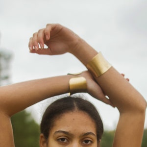 K&ouml;nnte beinhalten: Eine Person tr&auml;gt zwei goldene Armb&auml;nder an ihren Armen. Die Armb&auml;nder sind breit und flach und aus gl&auml;nzendem Metall gefertigt.