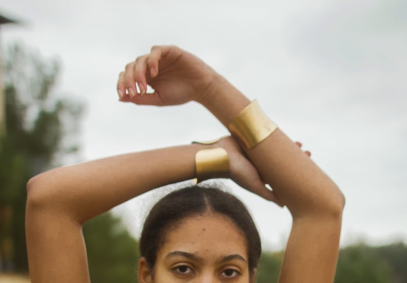 K&ouml;nnte beinhalten: Eine Person tr&auml;gt zwei goldene Armb&auml;nder an ihren Armen. Die Armb&auml;nder sind breit und flach und aus gl&auml;nzendem Metall gefertigt.