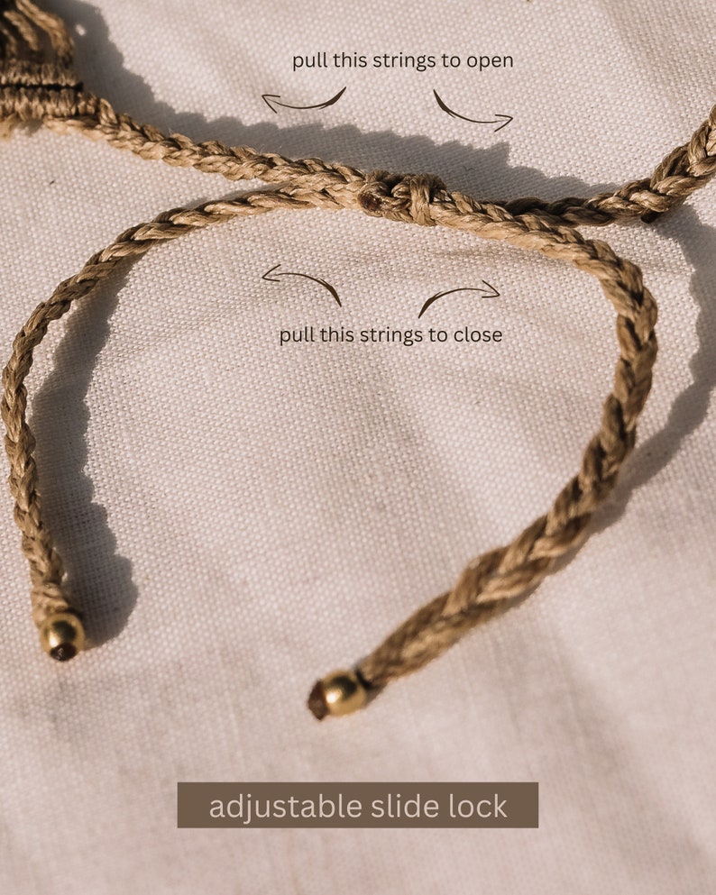May include: A brown braided cord bracelet with a gold adjustable slide lock. The bracelet is shown on a white fabric background. The text "pull this strings to open" and "pull this strings to close" is shown with arrows indicating how to open and close the bracelet.