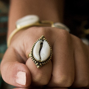 May include: A gold ring with a white seashell design. The ring is worn on a person's finger.