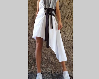 Puede incluir: Un vestido blanco con una faja negra y un panel a rayas gris y blanco en el hombro derecho. El vestido tiene un dobladillo asimétrico y se lleva con zapatillas blancas.
