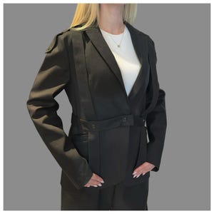 Front view of black denim blazer with eyelet details, long sleeves, and sculptural asymmetric strap elements.