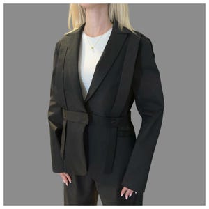 Women’s black designer blazer with architectural silhouette, asymmetric strap accents, and structured tailoring.