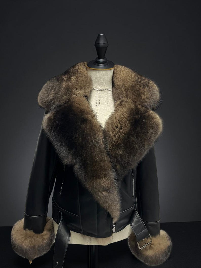 May include: Black leather jacket with a large brown fur collar and cuffs. The jacket has a belted waist and a zipper closure. The jacket is displayed on a mannequin.