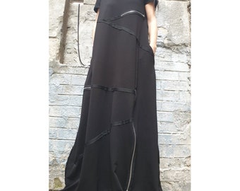 May include: A black maxi dress with short sleeves and a round neckline. The dress features diagonal panels with silver zippers and black ribbon accents. The dress has pockets and a flowing, wide skirt.